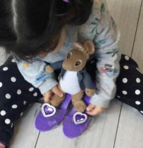 Young child playing with stuffed animal wearing matching purple slippers